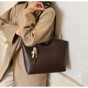 Detailed view of dark brown PU leather tote bag with beaded charm pendant and minimalist design.
