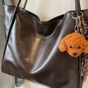 Detail view of brown oil-wax leather tote bag with cute fluffy poodle plush keychain charm.
