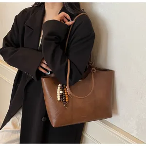 Details of brown leather tote bag with wooden bead charms, stylish minimalist underarm bag.