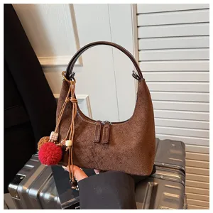 Brown suede mini dumpling handbag detail shot with furry pom-pom charm and top handle.