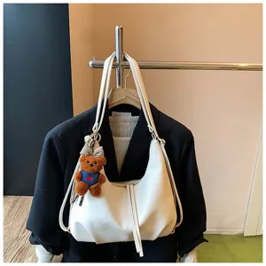 Detailed view of white PU leather slouchy shoulder bag with cute bear pendant, versatile design.