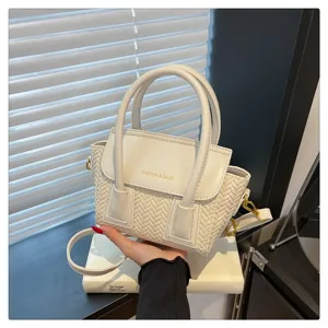 Detalle de bolso de mano blanco tejido, diseño de ala elegante con asas y correa.