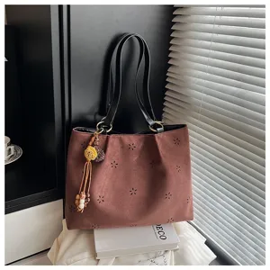 Detailaufnahme der herbstlichen Wildleder-Schultertasche mit Lochblumen und Quasten.