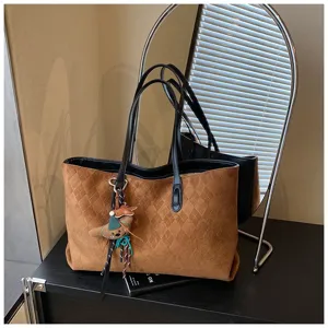 Close-up of brown suede quilted tote bag with black handles and cute plush pendant.