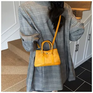 Close-up detail shot of yellow suede crossbody bag styled with a grey plaid blazer.