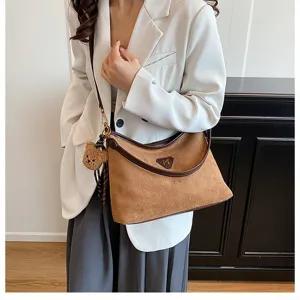 Detail shot of brown suede shoulder bag with chic bear pendant and elegant leather trim.