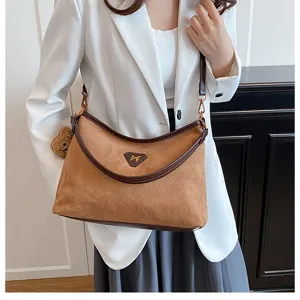 Brown suede shoulder bag detail showcasing contrast leather trim and cute bear pendant accessory.