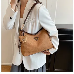 Close-up of brown suede shoulder bag detail, soft fabric, plush bear charm, elegant strap.