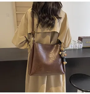 Detail shot of brown leather bucket shoulder bag with plush keychain for autumn and winter commuting.