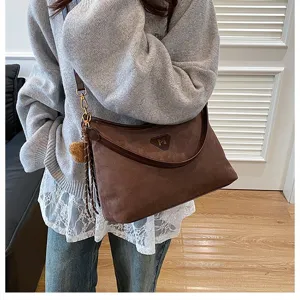 Brown suede underarm shoulder bag detail, soft fabric texture with delicate pom-pom charm.
