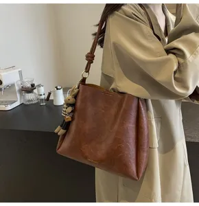 Stylish large capacity brown shoulder bucket bag with cute rabbit pendant for women commute.