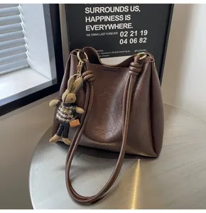 Detailed view of brown leather bucket shoulder bag with chic braided handle and cute rabbit charm.