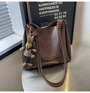 Detailed view of stylish brown leather shoulder bucket bag featuring cute rabbit pendant.