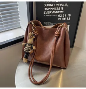 Brown leather shoulder bag detail showing premium texture and cute knitted rabbit charm.