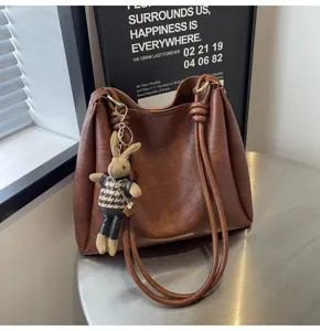 Brown leather shoulder bag for women, stylish large capacity bucket bag with cute rabbit charm.