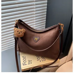 Detail view of dark brown suede shoulder bag featuring cute bear pendant and unique M logo.