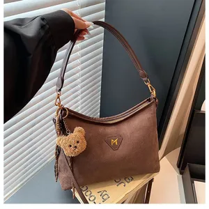 Brown suede shoulder bag detail showing soft texture, metal zipper and cute bear pendant.