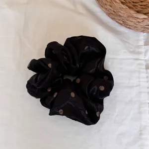 Primer plano detallado de un elegante coletero de seda negro con lunares marrones.