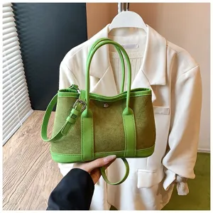 Detail shot of green suede patchwork shoulder bag with leather handles and metal hardware.