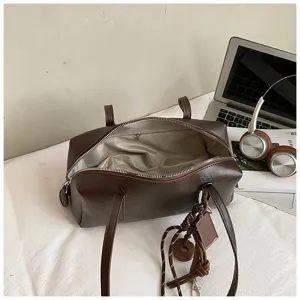 Detail shot of retro brown PU leather bowling shoulder bag with double handles and decor.