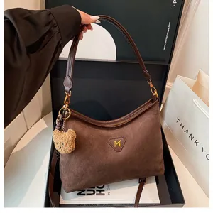 Brown suede shoulder bag detail showing premium texture, zipper closure and cute bear pendant.