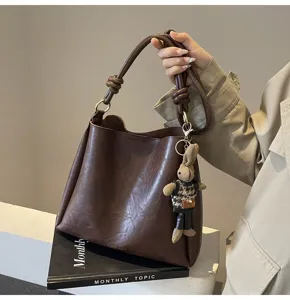 Stylish brown PU leather bucket bag with braided handle and cute rabbit pendant for autumn.