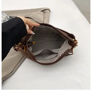 Brown suede shoulder bag interior detail showing black and white striped lining and zip pocket.