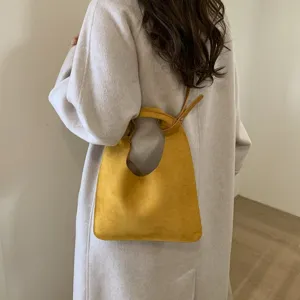 Detail view of a yellow suede shoulder bag carried by a woman wearing a long beige coat.