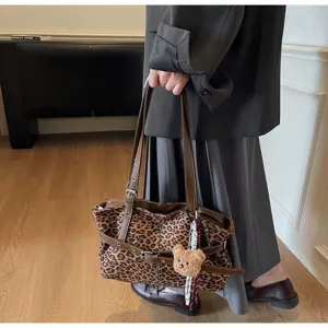 Detail of stylish leopard print commuter handbag featuring brown straps and cute bear charm.