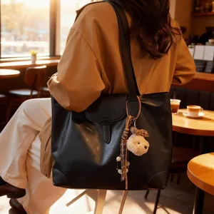 Detail shot of a retro black leather tote bag with plush charm in a cozy cafe setting.