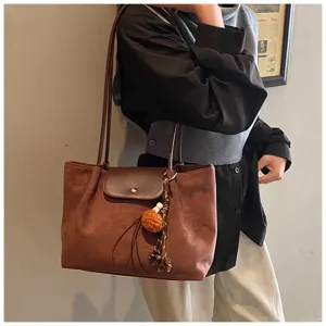 Detailed view of women's brown suede shoulder tote bag with flap and chic tassel charm.