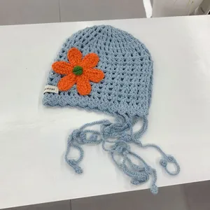 Close up of handmade crochet hollow knit beanie, light blue with vibrant orange flower detail.