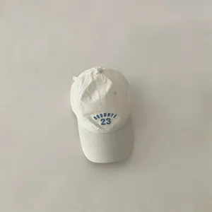 Detail shot of white kids baseball cap featuring blue embroidered lettering on the front.