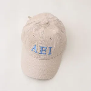Corduroy kids baseball cap detail view, featuring blue embroidered AEI letters on beige fabric.