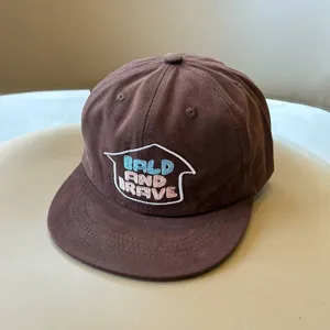 Primer plano de gorra de béisbol marrón para niños con letras bordadas, detalle de algodón