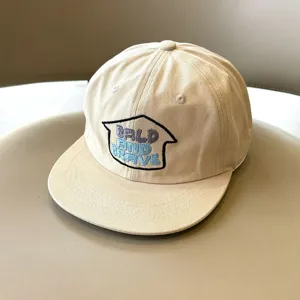 Detalle de una gorra de beisbol beige para ninos con eslogan bordado y visera plana.