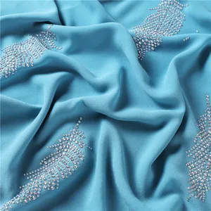 Lichtblauwe chiffon sjaal detail met sprankelende strass bladpatronen en zachte val.