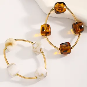 Detailansicht stilvoller stapelbarer Perlenarmbänder mit Golddraht und quadratischen Harzanhängern.