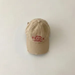 Detail view of the beige cotton baseball cap, featuring distressed brim and red embroidery.