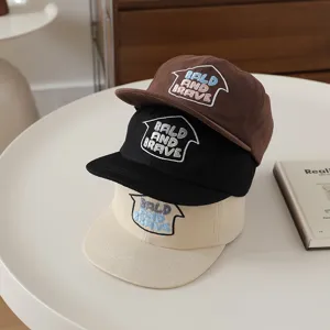 Close-up of stacked kids flat brim caps in brown, black, and beige with embroidery.