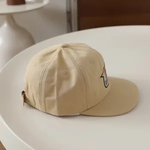 Detailed side view of beige kids flat brim baseball cap with cute cartoon embroidery.