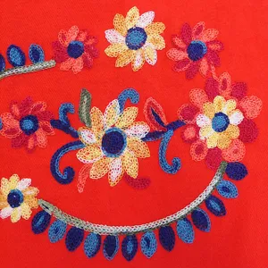 Detailed view of traditional ethnic style embroidered floral pattern on warm red cashmere feel scarf.