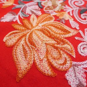 Close-up detail of embroidered floral pattern on red imitation cashmere scarf fabric.