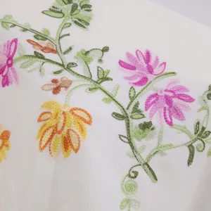 Close-up detail of exquisite colorful floral and vine embroidery on soft white fabric.