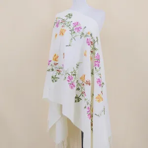 Close-up of delicate colorful floral vine embroidery on soft white shawl fabric texture.