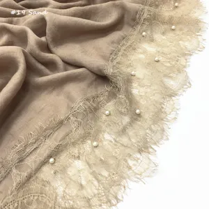 Detailopname van de beige katoenen linnen sjaalrand met fijn kant en witte parels.