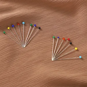Dettaglio in primo piano di spille con capocchia in vetro colorato disposte per la sartoria.