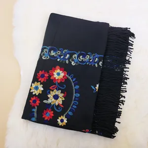 Close-up detail of black cashmere-feel shawl with colorful floral embroidery and fringe edge.