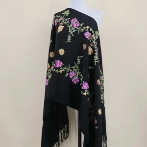 Closeup view of the black cashmere-feel shawl featuring delicate colorful floral embroidery and fringe.