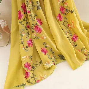 Detail shot of lightweight yellow floral embroidered scarf, soft fabric with pink flowers and green vines.